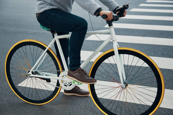 Vista lateral de cara irreconhecível em roupa casual andar de bicicleta com smartphone no guidão montar perto de passarela na estrada da cidade
 - Foto, Imagem