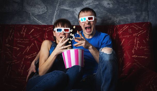 A couple of guy and girl watch a scary movie in 3D glasses and scream with fright. Popcorn. - Foto, afbeelding