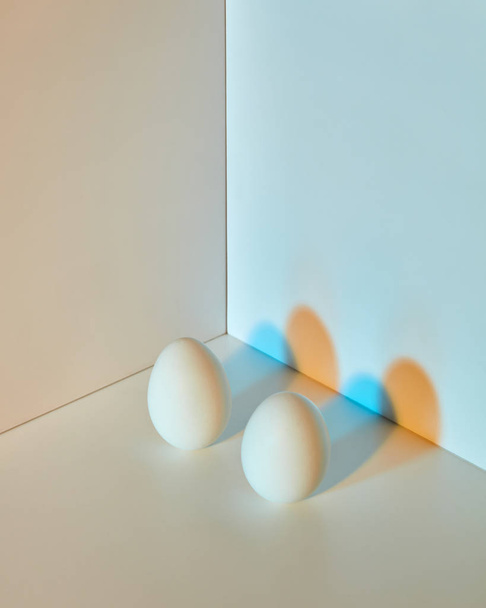 Two eggs on double gray-blue background with a reflection of orange-blue shadows and space for text. Easter. - Fotografie, Obrázek