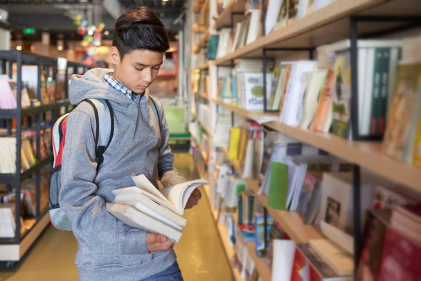 Koulupoika seisoo tilalla kirjoja selailu läpi keskittyen
 - Valokuva, kuva