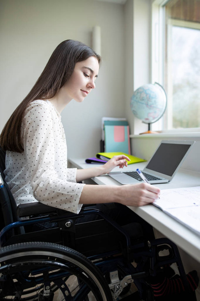 Adolescente chica en silla de ruedas estudiando en casa en el ordenador portátil
 - Foto, imagen