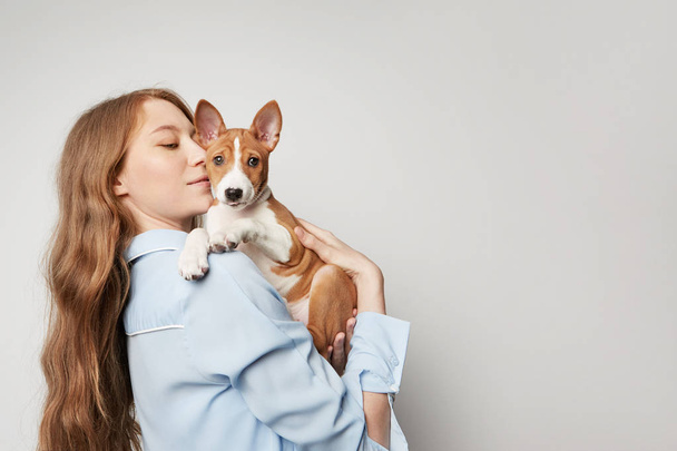 Cute young woman hugging and kissing her puppy basenji dog. Love between dog and owner. Isolated on white background - Фото, изображение