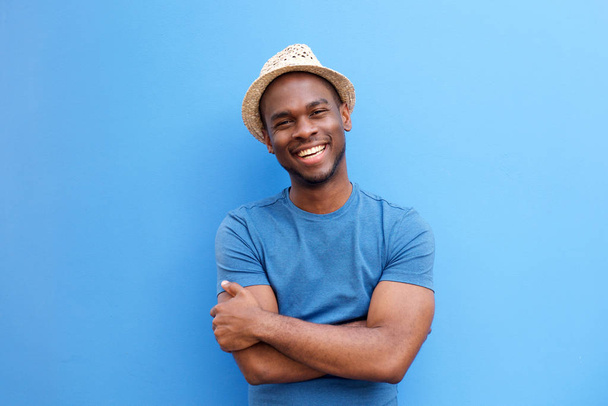 Portret van knappe jonge zwarte jongen lachend met hoed tegen blauwe achtergrond - Foto, afbeelding