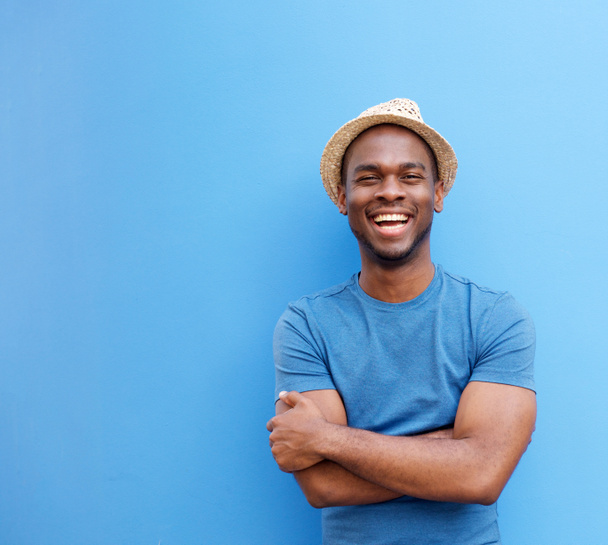Porträt eines hübschen jungen Schwarzen mit Hut, der vor blauem Hintergrund lächelt - Foto, Bild