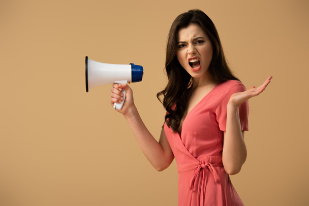 Boos brunette vrouw in jurk bedrijf megafoon en schreeuwen geïsoleerd op beige - Foto, afbeelding