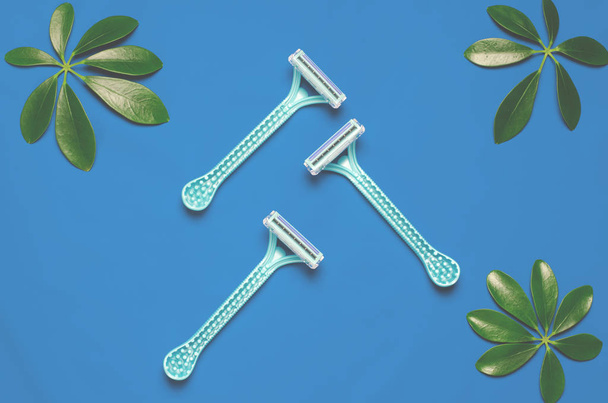 shaving razor lie on the colored background next to green leaves - Photo, Image