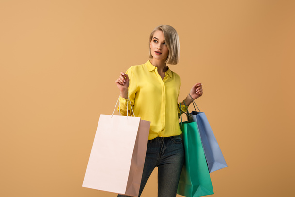 Pensive blonde girl in yellow shirt holding shopping bags isolated on beige - Fotografie, Obrázek