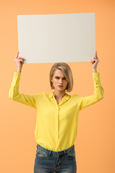 Chica rubia insatisfecha con camisa amarilla sosteniendo cartel en blanco aislado en naranja
 - Foto, Imagen