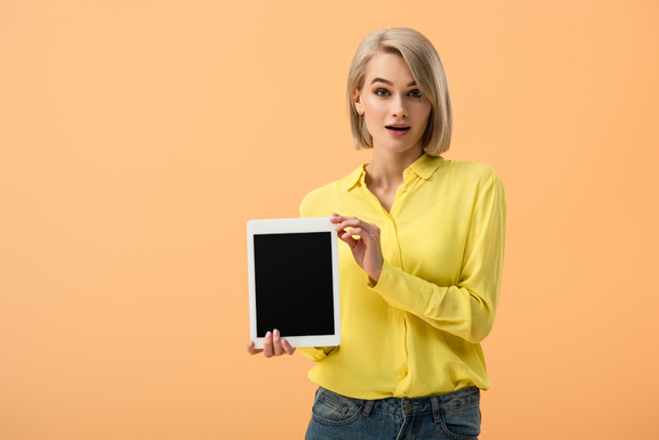 Surprised girl in yellow shirt holding digital tablet with blank screen isolated on orange - Photo, Image