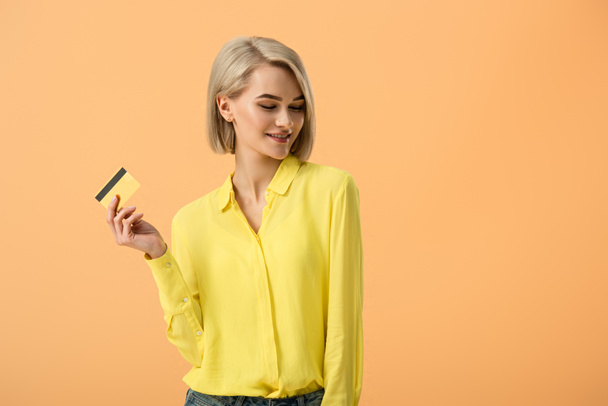 Uroczy Kobieta blonde w żółta Koszulka posiadania karty kredytowej na pomarańczowym tle - Zdjęcie, obraz
