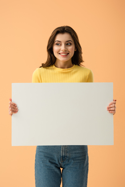 Blissful smiling brunette girl holding blank placard isolated on orange - Fotoğraf, Görsel