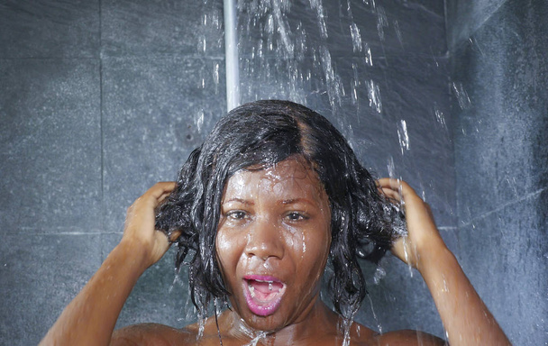 Porträt einer jungen glücklichen und schönen schwarzafrikanischen Amerikanerin, die glücklich lächelt und zu Hause duscht. Badezimmer, in dem sie sich die Haare mit Shampoo wäscht - Foto, Bild