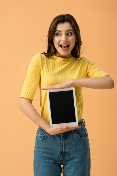 Excited young woman holding digital tablet with blank screen isolated on orange - 写真・画像