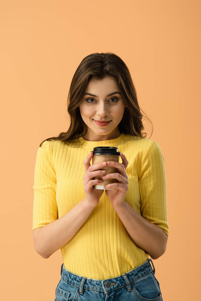 Front view of tricky brunette girl holding paper cup of coffee isolated on orange - Фото, изображение