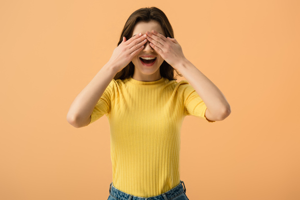 cheerful young woman covering eyes with hands isolated on orange  - Fotografie, Obrázek
