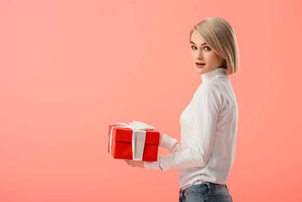 surprised blonde woman holding gift box in hands isolated on pink  - Φωτογραφία, εικόνα