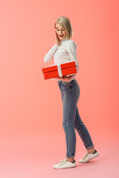 schockierte blonde Frau schaut auf Geschenkbox auf rosa Hintergrund - Foto, Bild