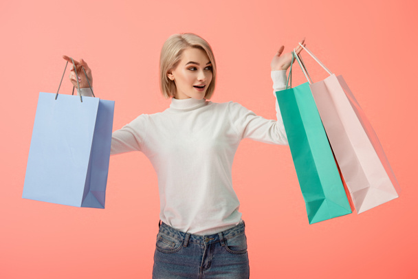 surprised blonde young woman holding shopping bags isolated on pink   - Valokuva, kuva