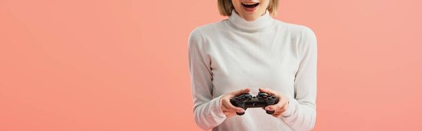 panoramic shot of surprised girl holding joystick while standing isolated on pink  - Фото, изображение