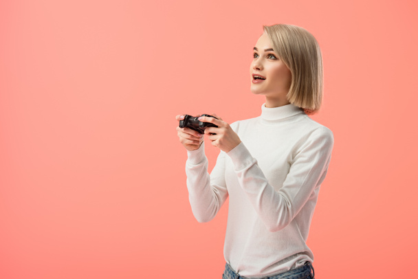 surprised blonde woman holding joystick while playing isolated on pink  - Фото, зображення