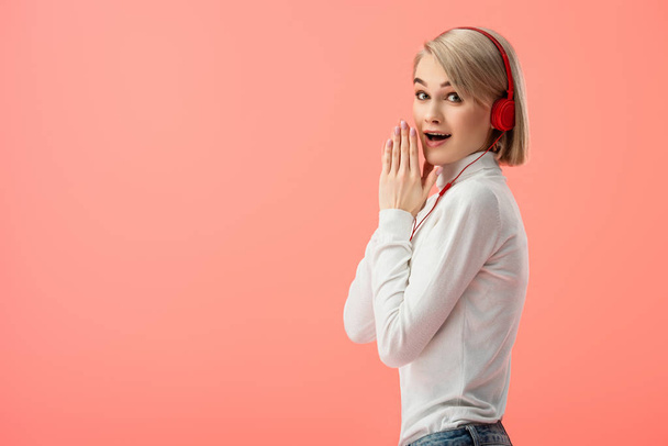 shocked blonde woman listening music in headphones isolated on pink  - Foto, immagini