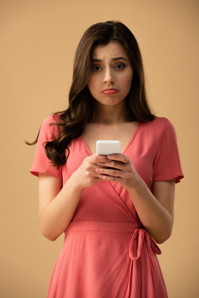upset brunette girl holding smartphone isolated on brown  - Photo, Image