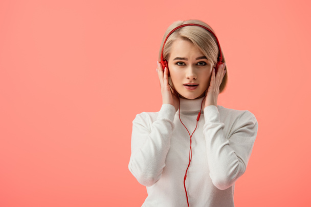здивована блондинка молода жінка слухає музику в навушниках ізольовано на рожевому
  - Фото, зображення