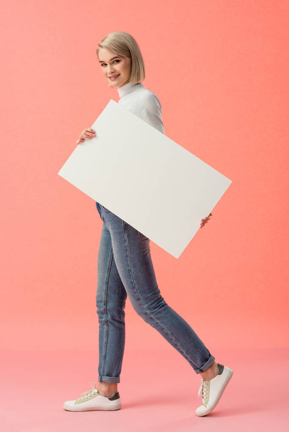 cheerful blonde woman holding blank placard on pink background  - Foto, afbeelding