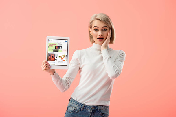 surprised blonde woman holding digital tablet with ebay app on screen isolated on pink  - Foto, Imagem