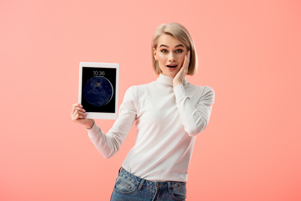 здивований блондинка Жінка тримає цифровий планшет з екрану блокування ізольовані на рожевий  - Фото, зображення