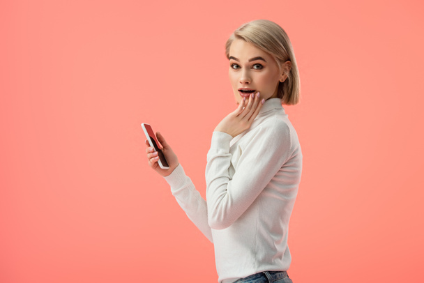 surprised blonde girl using smartphone isolated on pink  - Foto, imagen