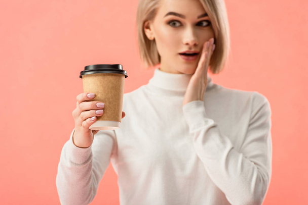 surprised blonde girl looking at paper cup isolated on pink  - Foto, Imagen
