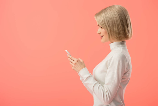 vista laterale di attraente donna bionda utilizzando smartphone isolato su rosa
 - Foto, immagini