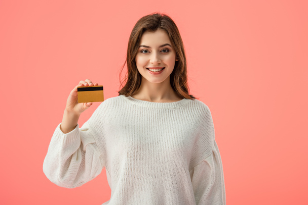 smiling brunette girl holding credit card isolated on pink - Photo, image