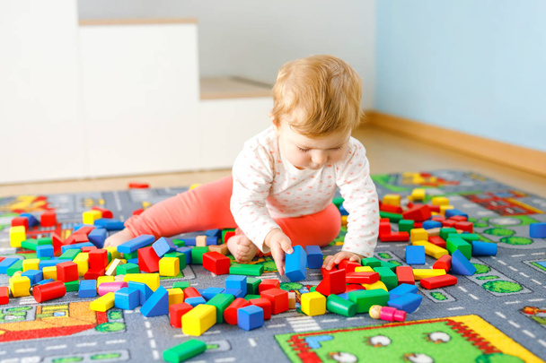 Чарівна дівчинка грає з освітніми іграшками. Щаслива здорова дитина розважається з різнокольоровими дерев'яними блоками вдома в домашній кімнаті. Дитячі кольори та форми навчання
 - Фото, зображення