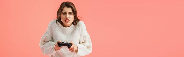 panoramic shot of brunette girl holding joystick while playing isolated on pink  - Fotó, kép