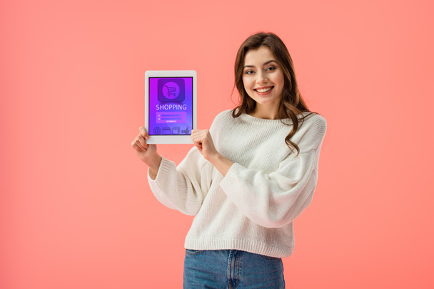 cheerful young woman holding digital tablet with shopping app on screen isolated on pink  - Foto, Imagen