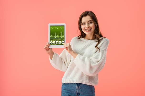 happy young woman holding digital tablet with health app on screen isolated on pink  - Фото, изображение