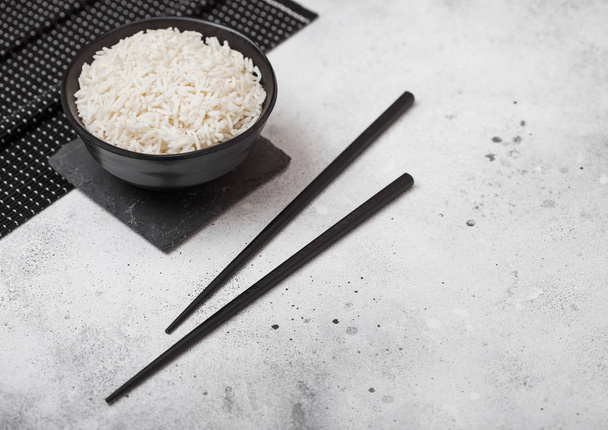 Black bowl with boiled organic basmati jasmine rice with black chopsticks on bamboo placemat on light kitchen table  background. Space for text - Foto, Imagem
