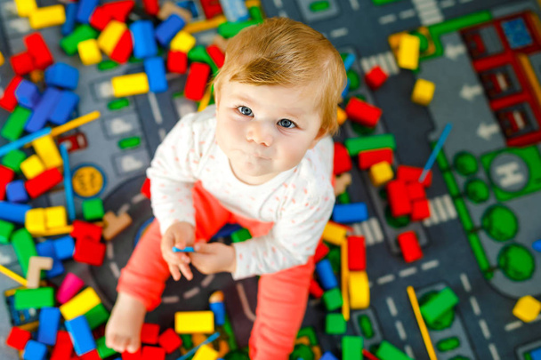 Очаровательная девочка играет с образовательными игрушками. Счастливый здоровый ребенок веселится с разноцветными деревянными блоками дома в домашней комнате. Детское обучение цветов и форм - Фото, изображение