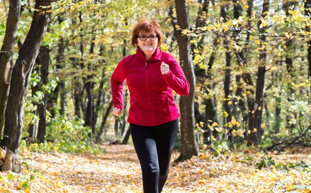 Donna di mezza età che indossa abbigliamento sportivo e corre nella foresta
 - Foto, immagini