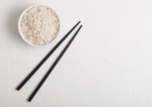 White bowl with boiled organic basmati jasmine rice with black chopsticks on white background. Space for text - Foto, Imagem