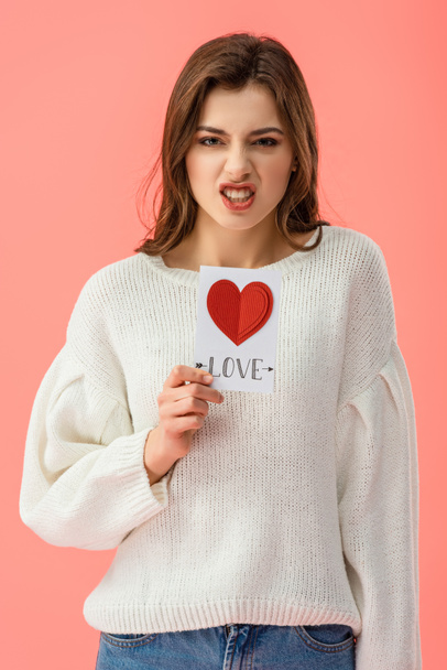 angry young woman holding card with love lettering isolated on pink   - Фото, зображення