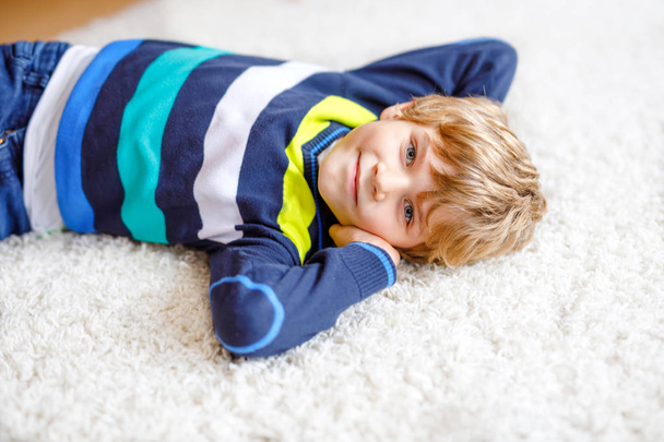 Portrait of little cute kid boy against white background. Boy lying on ground and looking at the camera. Child wearing colorful fashion kids clothes - Фото, изображение