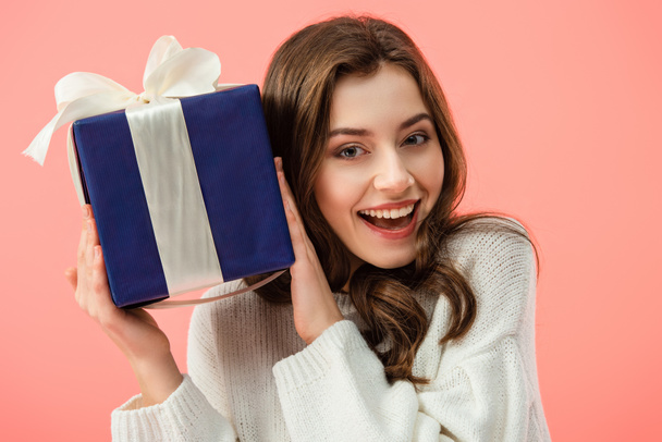 smiling and beautiful woman in white sweater holding gift box isolated on pink  - Zdjęcie, obraz