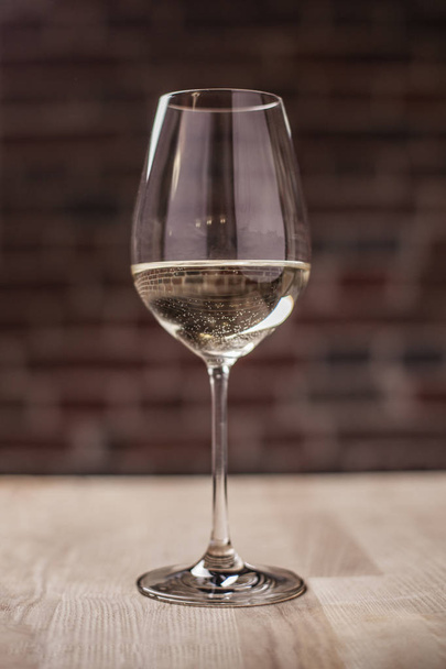 white semi-sweet grape naturally tasty wine in an elegant glass goblet stands on a wooden table in a restaurant. A great addition to dinner - Photo, Image