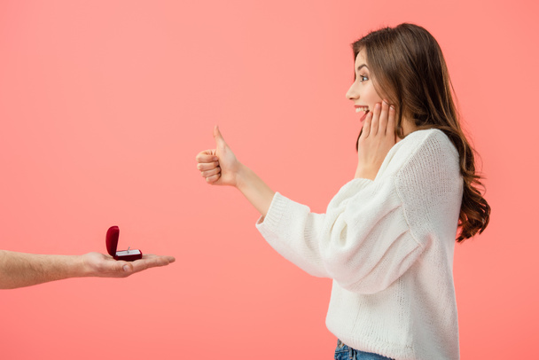 Cropped view of man making marriage proposal to surprised brunette girl with thumb up isolated on pink - Fotografie, Obrázek