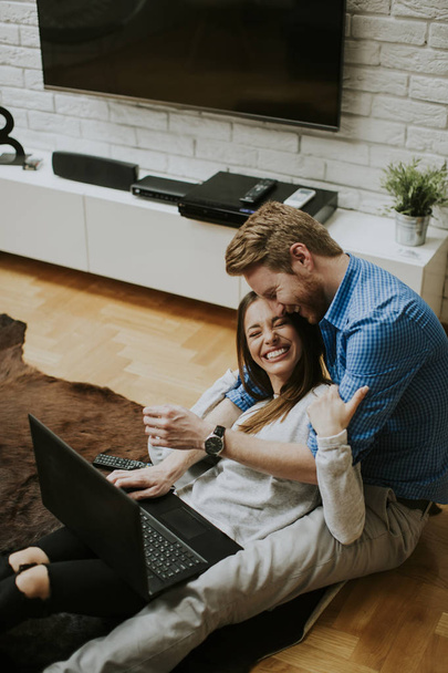 Close-up vista no jovem casal usando laptop enquanto sentado no chão em sua sala de estar
 - Foto, Imagem