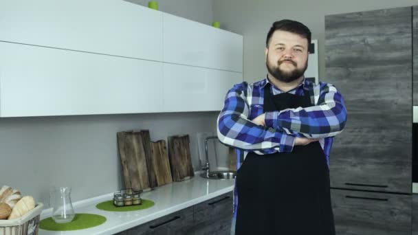 Thick bearded man as a cook wearing apron is in a modern kitchen and looks into the camera - Video