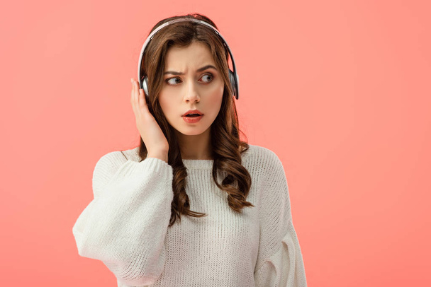 σοκαρισμένος και ελκυστική γυναίκα στο λευκό πουλόβερ με ακουστικά που απομονώνονται σε ροζ - Φωτογραφία, εικόνα